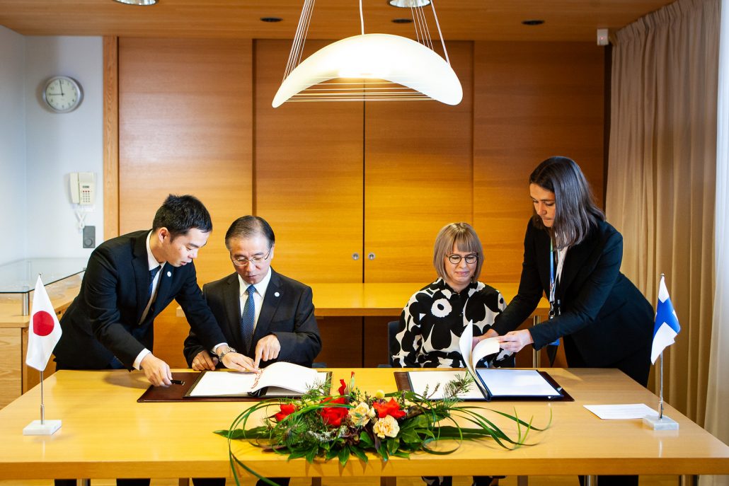 Sosiaali- ja terveysministeri Aino-Kaisa Pekonen ja Japanin Suomen-suurlähettiläs Takashi Murata allekirjoittavat sosiaaliturvasopimusta pöydän ääressä. Kuvassa myös heidän avustajansa. 